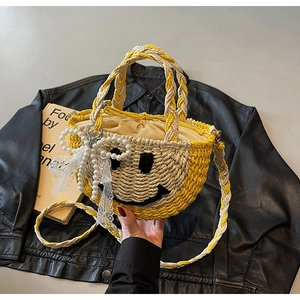 Detail view of woven straw bag with a black stitched smiley face and pearl bow accessory