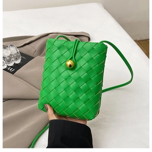 Detail of green woven crossbody bag featuring a signature gold spherical buckle closure