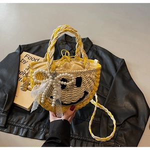 Detail of straw woven bag with yellow smiley face, pearl bow, and lace trim on black leather