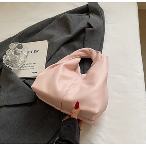 Detail of a light pink pleated cloud bag with a knotted handle on a soft fabric backdrop