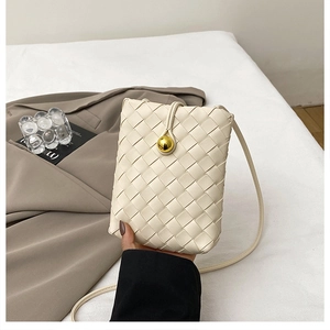 Detail of cream woven leather crossbody bag featuring a unique gold sphere buckle closure