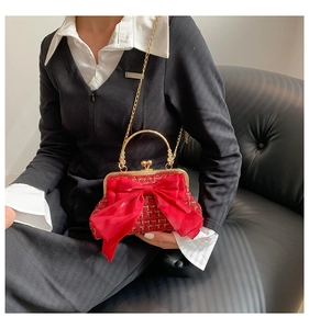 Detail of red tweed clutch bag with large silk bow and gold chain on model