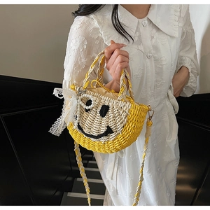 Detail of hand-woven straw bag featuring a black smiley face, lace bow, and pearl strap