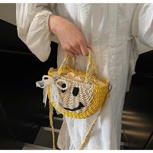 Detail of straw bag with yellow smile face design, pearl charm, and woven strap