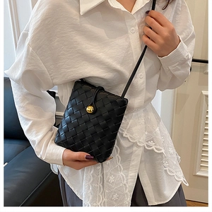 Detail of black woven crossbody bag with gold buckle on white lace shirt model