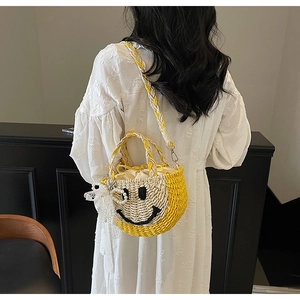 Detailed view of straw bucket bag with smiling face, lace pendant and pearl charm