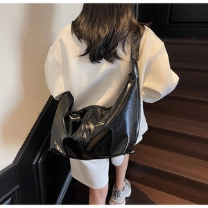 Vue détaillée du grand sac à bandoulière noir brillant porté sur une tenue blanche