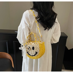Detail of hand-woven straw bucket bag with smiley face pattern and pearl charm