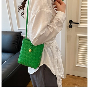 Detailed view of green woven bucket bag featuring a striking gold sphere clasp and strap