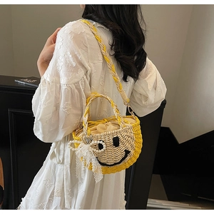 Detail of straw bucket bag featuring embroidered smiley face and decorative pearl bow