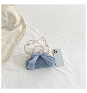 Close-up of light blue tweed chain bag featuring a large bow and gold round handles