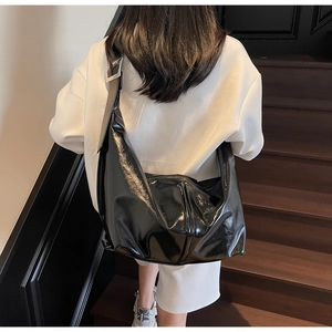 Détail d'un sac hobo noir brillant avec boucle argentée sur bandoulière large