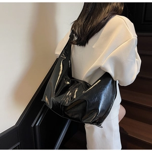 Détail d'un sac hobo en cuir verni brillant noir avec large bandoulière porté par un mannequin