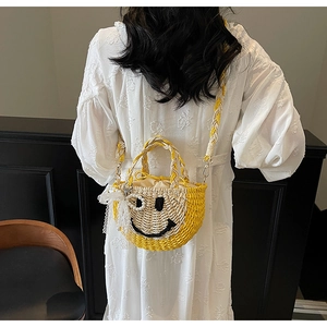 Detail of straw bucket bag with smiley face and lace pearl pendant on white dress
