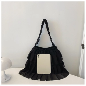 Detail of black tiered ruffle shoulder bag with chiffon textures next to an iPad