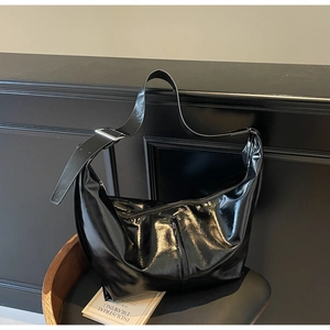 Détail d'un sac hobo en cuir verni noir avec boucle argentée sur une chaise en bois