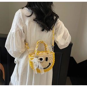 Detail of handmade straw crossbody bag featuring a lace bow and black stitched smiley face