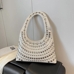Minimalist beige hobo bag with silver studs in a radial pattern on a black leather bench