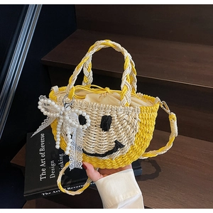 Detail of straw woven bucket bag featuring a black smiley face and pearl bow ornament