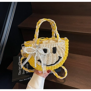 Detail of hand-woven straw bag featuring black smile design and pearl lace bow charm