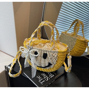 Detail of straw bucket bag with smiley face embroidery and pearl lace bow accessory