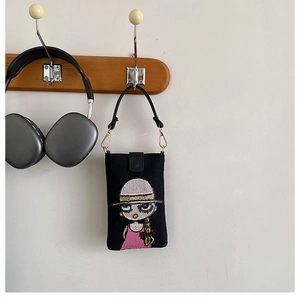 Détail du sac à téléphone en toile noire avec broderie fille et crochets dorés