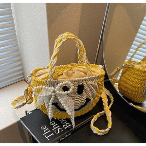 Detail of straw bucket bag featuring a black smiley face, pearl bow and lace charms