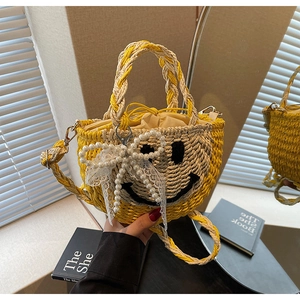 Detail of hand-woven straw bag with smiling face embroidery and pearl bow charm