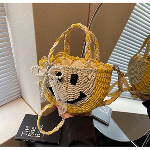 Close-up of straw woven bag featuring a black smiley face and pearl lace bow ornament