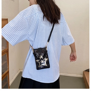 Détail d'un sac bandoulière noir à paillettes avec une grande étoile sur une chemise à carreaux