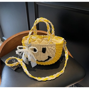 Detail of yellow woven bucket bag with smiling face embroidery and lace pearl pendant