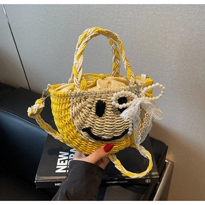 Detail of straw woven bag featuring black smiley face embroidery and pearl bow charm