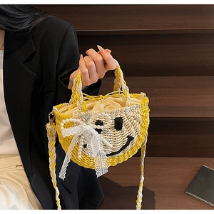 Close-up of yellow straw beach bag with smiley face pattern and lace bow detail