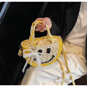 Detail of straw bag with embroidered smiley face, white lace bow, and pearl chain strap