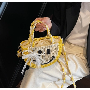 Detail of hand-woven straw bag with black embroidered smiley face and pearl lace bow