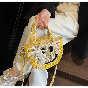 Detail of yellow straw bag with embroidered smiley face, lace bow and pearl charms