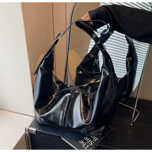 Détail du sac hobo noir brillant avec large bandoulière sous un éclairage de fenêtre doux