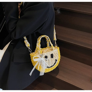Detail of hand-woven straw bag featuring a yellow smiley face and lace bow detail