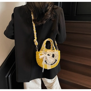 Detail of yellow straw bag with black smile and lace bow on a crossbody strap