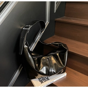 Détail d'un sac hobo en cuir brillant noir avec boucle en métal argenté et bandoulière large