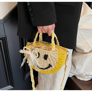 Detail of yellow straw bag with smiley face pattern, lace bow and pearl charm accents