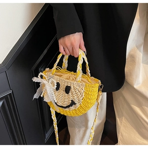 Detail of hand-woven straw bag featuring black smiley face pattern and lace pearl charm