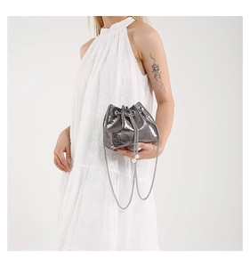 Close-up of silver bucket bag with skull embossment and pearl chain on a white dress