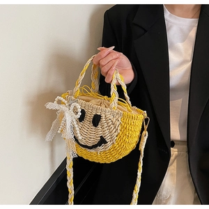 Detail of hand-woven straw bucket bag featuring a black smiley face and pearl lace bow
