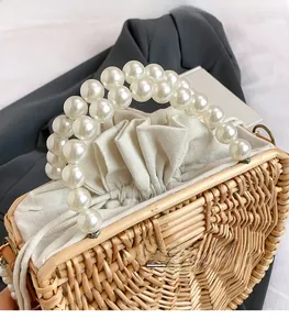 Detail of handmade woven bamboo bag featuring luxury pearl handles and linen drawstring liner