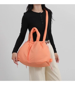 Detail of quilted puffer tote featuring padded handles and drawstring closure in coral