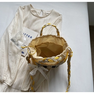 Detailed macro view of woven straw bucket bag with pearl charms and lace bow decorations