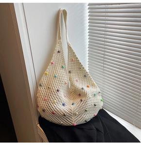 Detailed close-up of white crochet knit shoulder bag with colorful pearls on a windowsill