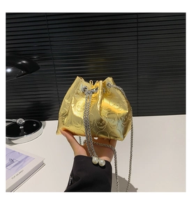 Detail of gold skull-embossed bucket bag with silver chain strap and pearl accents