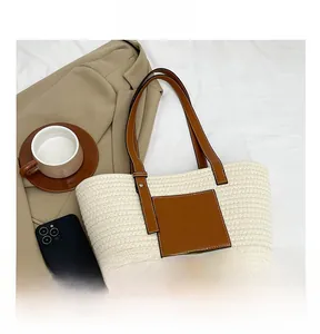 Detail of straw woven tote bag featuring brown leather pocket and long shoulder straps